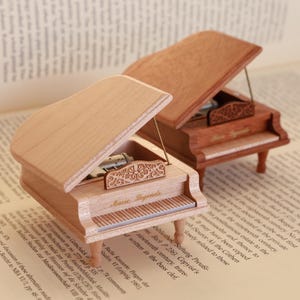 May include: Two wooden music boxes shaped like grand pianos. The music boxes are open and the intricate mechanisms are visible. The music boxes are sitting on a book with text.