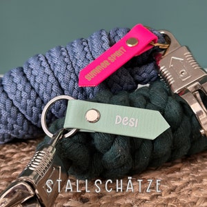 Könnte beinhalten: Zwei geflochtene Schlüsselbänder aus Seil mit Lederanhängern. Das blaue Schlüsselband hat einen rosa Anhänger mit der Aufschrift "Summer Spirit" und das grüne Schlüsselband hat einen hellgrünen Anhänger mit der Aufschrift "Desi".