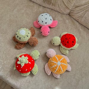 Puede incluir: Cinco tortugas hechas a mano con ganchillo con caparazones con temática de frutas. Las tortugas presentan caparazones diseñados para parecerse a una sandía, fresa, kiwi, naranja y una fruta blanca y negra. Las tortugas tienen cuerpos rosas, verdes y marrones.