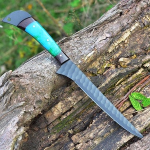 K&ouml;nnte beinhalten: Ein schwarzes und blaues Messer mit einer strukturierten Klinge und einem blauen und schwarzen Griff. Das Messer liegt auf einem St&uuml;ck Holz.