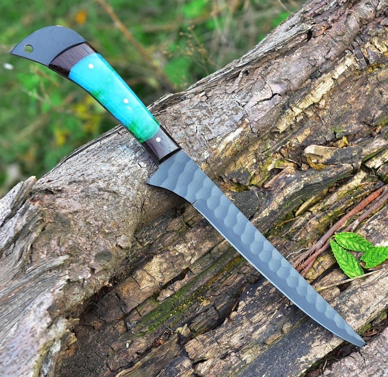 K&ouml;nnte beinhalten: Ein schwarzes und blaues Messer mit einer strukturierten Klinge und einem blauen und schwarzen Griff. Das Messer liegt auf einem St&uuml;ck Holz.