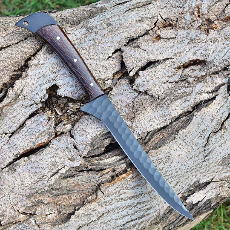K&ouml;nnte beinhalten: Ein schwarzes und braunes K&uuml;chenmesser mit einer strukturierten Klinge und einem Holzgriff. Das Messer liegt auf einem St&uuml;ck Baumrinde.