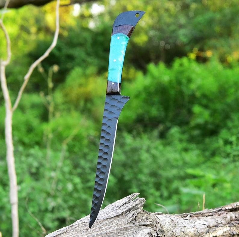 K&ouml;nnte beinhalten: Ein schwarzes und blaues Filetiermesser mit einer strukturierten Klinge und einem t&uuml;rkisfarbenen und schwarzen Griff. Das Messer steht aufrecht auf einem St&uuml;ck Holz.