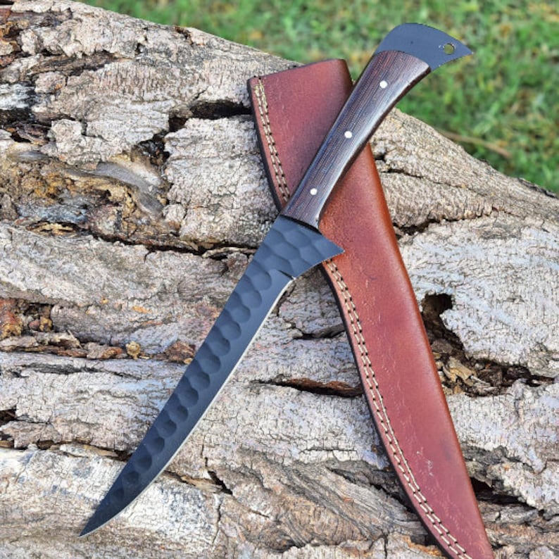 K&ouml;nnte beinhalten: Ein schwarzes Messer mit einer strukturierten Klinge und einer braunen Lederscheide. Das Messer hat einen Holzgriff mit schwarzer Oberfl&auml;che.