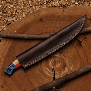 K&ouml;nnte beinhalten: Eine braune Lederscheide mit einem gen&auml;hten Muster. Das Messer hat einen blau-wei&szlig;-roten Griff mit einem Sternmuster.