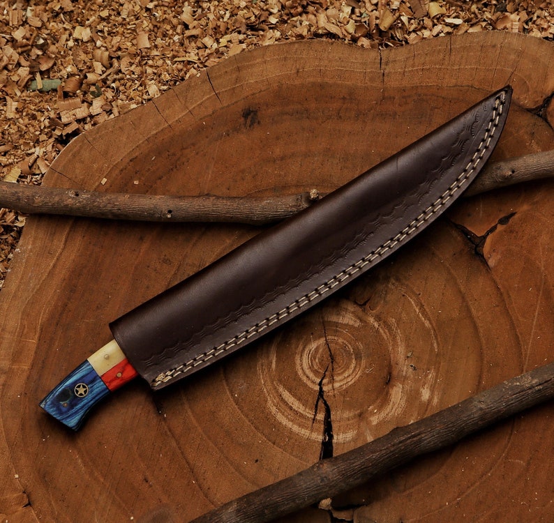 K&ouml;nnte beinhalten: Eine braune Lederscheide mit einem gen&auml;hten Muster. Das Messer hat einen blau-wei&szlig;-roten Griff mit einem Sternmuster.