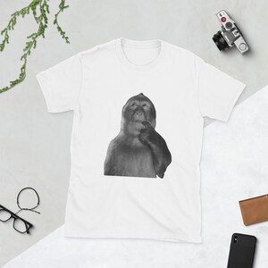 Peut inclure: T-shirt blanc avec une image en noir et blanc d'un singe pensif. Le t-shirt a un col rond et est fait d'un tissu doux. Un style unisexe.