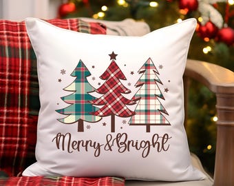 Puede incluir: Cojín cuadrado blanco con tres árboles de Navidad a cuadros en verde azulado, rojo y crema. El cojín tiene las palabras "Merry & Bright" en una fuente marrón. El cojín está sobre una silla con una manta a cuadros rojos.