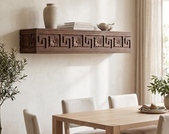 May include: A rectangular dark brown wooden floating shelf mounted on a wall, featuring a repeating carved pattern of geometric Greek key motifs interspersed with square floral medallions along its front face.