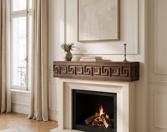 May include: A fireplace featuring a dark brown wooden mantel with a carved Greek key pattern and floral motifs. The fireplace surround is made of light beige stone, framing a black firebox with burning logs and visible orange flames.