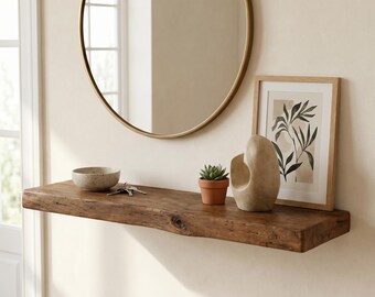 May include: A rustic wooden floating shelf with a natural live edge, featuring a speckled ceramic bowl, a set of metal keys, a small green succulent in a terracotta pot, a smooth beige abstract sculpture, and a framed botanical print.
