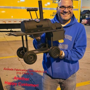 May include: A black metal barbecue grill with a smoker, side shelf, and wheels. The grill has a temperature gauge and is held by a person. The text "Andrade Fabrication Specialists LLC" and "Another Happy Customer!" is visible.