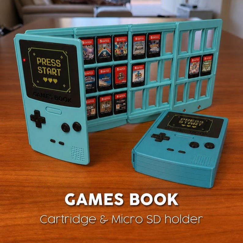 Op de afbeelding: Een lichtblauwe Games Book cartridge- en micro SD-kaarthouder, ontworpen als een retro handheld gameconsole. De houder is open en toont verschillende game cartridges. De tekst "PRESS START" is zichtbaar aan de voorkant.