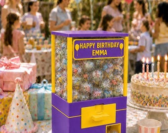 May include: A purple and yellow vending machine filled with clear plastic capsules. The front panel features a yellow sign with the text HAPPY BIRTHDAY EMMA and balloon icons. The machine has a dispensing slot at the bottom with a single capsule.