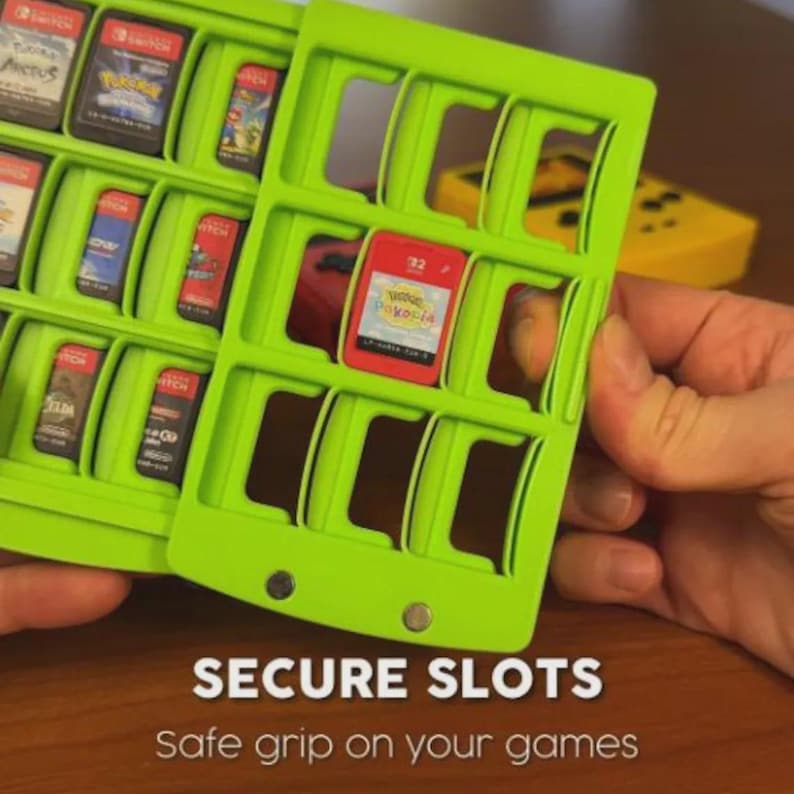 Op de afbeelding: Een felgroene spelcartridgehouder met meerdere sleuven, waarvan sommige spelcartridges bevatten. De houder wordt door een persoon vastgehouden. De tekst "SECURE SLOTS" en "Safe grip on your games" is zichtbaar.