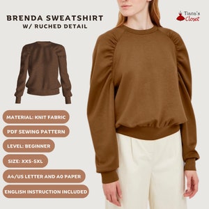 May include: A brown sweatshirt with a gathered detail on the shoulders. The sweatshirt has a crew neck and long sleeves. The text "BRENDA SWEATSHIRT W/ RUCHED DETAIL" is at the top of the image. The text "Tiana's Closet" is at the top right of the image. The text "MATERIAL: KNIT FABRIC", "PDF SEWING PATTERN", "LEVEL: BEGINNER", "SIZE: XXS-5XL", "A4/US LETTER AND A0 PAPER", and "ENGLISH INSTRUCTION INCLUDED" is at the bottom of the image.
