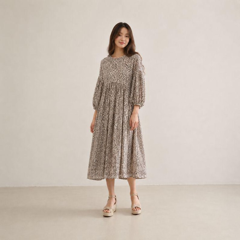 May include: A midi-length dress featuring a brown and white animal print pattern, a round neckline, and long puff sleeves with gathered cuffs. The dress has a fitted bodice that transitions into a loose, flowing skirt that falls below the knees.
