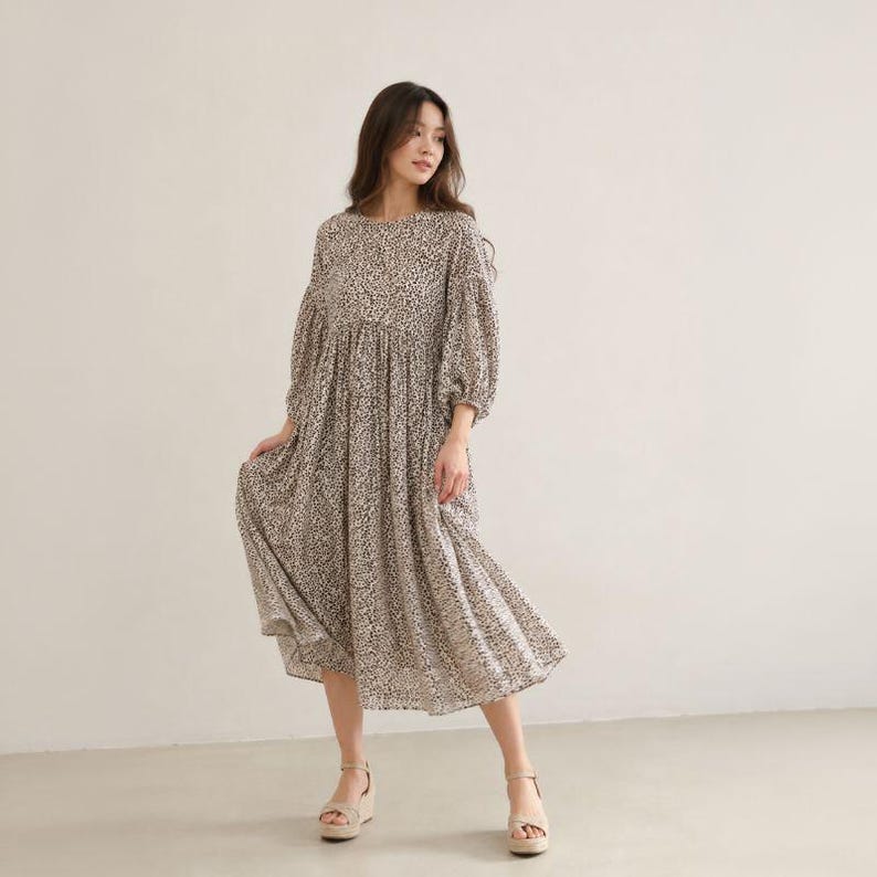 May include: A midi-length dress featuring a round neckline, long puff sleeves with elasticated cuffs, and a loose, flowing silhouette. The garment is made of a lightweight fabric with an all-over small-scale black and white animal print pattern.