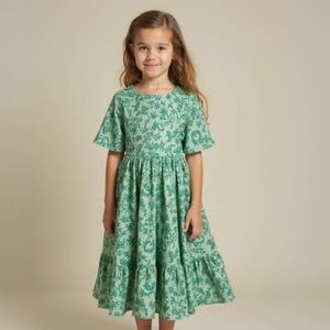 May include: A green floral print dress with a round neckline and short sleeves. The dress has a gathered waist and a tiered skirt.