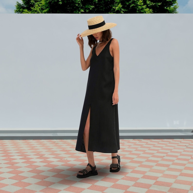 May include: A woman wearing a black maxi dress with a side slit and a straw hat. She is standing on a checkered tile floor.