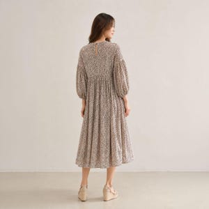 May include: A midi-length dress featuring a small-scale black and white animal print pattern. The garment has long, voluminous puff sleeves, a high round neckline with a small back button closure, and a gathered waistline that flows into a full skirt.