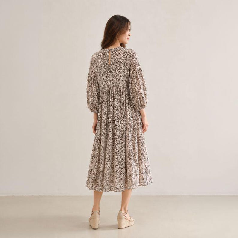 May include: A midi-length dress featuring a small-scale black and white animal print pattern. The garment has long, voluminous puff sleeves, a high round neckline with a small back button closure, and a gathered waistline that flows into a full skirt.