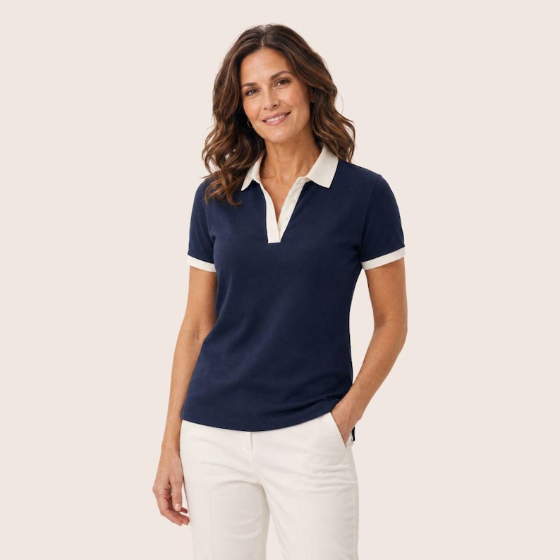 May include: A navy blue short-sleeved polo shirt featuring a white collar and white trim on the sleeve cuffs. The shirt has a deep V-neckline with a white placket detail and is paired with white trousers, creating a clean and simple look.