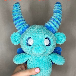 May include: A crocheted blue and white plush toy with large eyes and horns. The toy is being held by a hand. The text "PDF PATTERN ONLY" is visible at the top of the image.