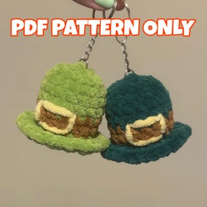 May include: Two plush green and teal leprechaun hat keychains with brown and cream accents. The keychains are attached to silver chains. The text "PDF PATTERN ONLY" is displayed in orange and white letters at the top of the image.