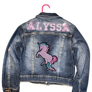 May include: A blue denim jacket with a pink unicorn patch and the name "ALYSSA" in pink letters on the back.