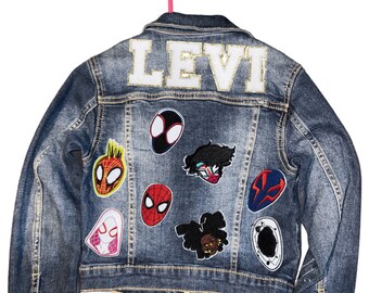 May include: A blue denim jacket with the name "LEVI" embroidered on the back in white with gold glitter. The jacket has several colorful patches sewn on the back, including Spider-Man characters.