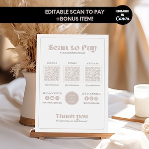 May include: A white sign with the text "Scan to Pay" in a pink, retro font. The sign includes QR codes for Google Pay, Venmo, and Cash App, along with the text "Your Business Name". The sign also includes the text "Also Accepted: cash, credit, apple pay" and a space for a logo. The sign is on a wooden stand and is in front of a white surface.