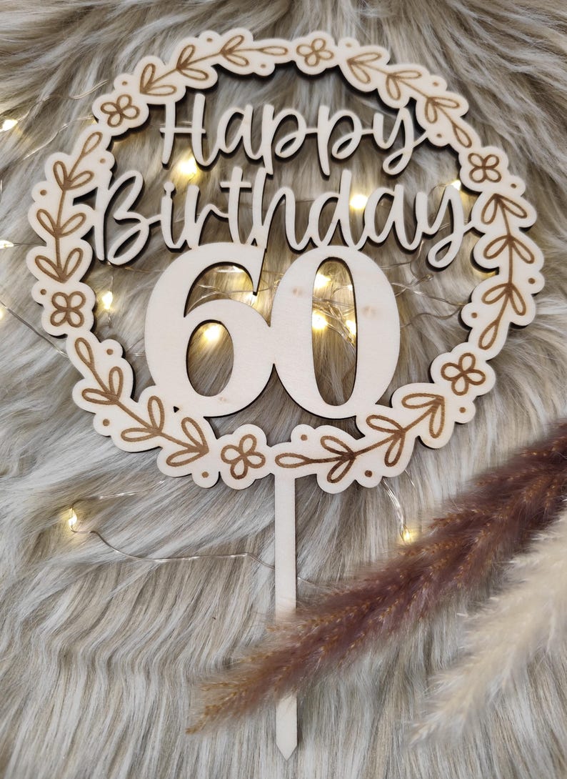 May include: Wooden cake topper with a floral wreath design. The topper says "Happy Birthday 60" in a white script font.