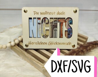 May include: A wooden plaque with the word "NICHTS" cut out, revealing images of Euro banknotes. The plaque has the phrases "Du wolltest doch" and "Herzlichen Glückwunsch" engraved. Gold-coloured rivets secure the plaque.