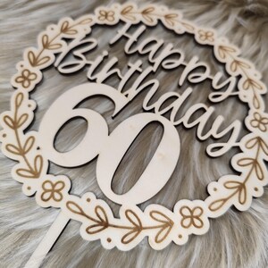 May include: Wooden cake topper with a floral wreath design and the text "Happy Birthday 60".