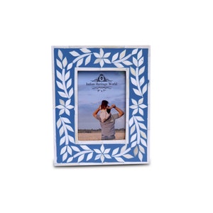 May include: A blue picture frame with a white floral design. The frame is made of bone and has a rectangular shape. The frame is 5 x 7 inches.
