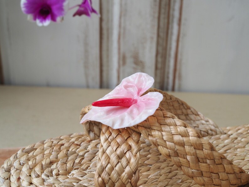 May include: A pair of woven straw sandals with a pink and red flower embellishment.