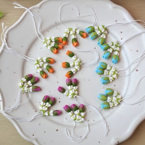 May include: A set of ten flower garlands with white jasmine flowers and colorful rose buds. The garlands are tied with white string and are arranged on a white plate.