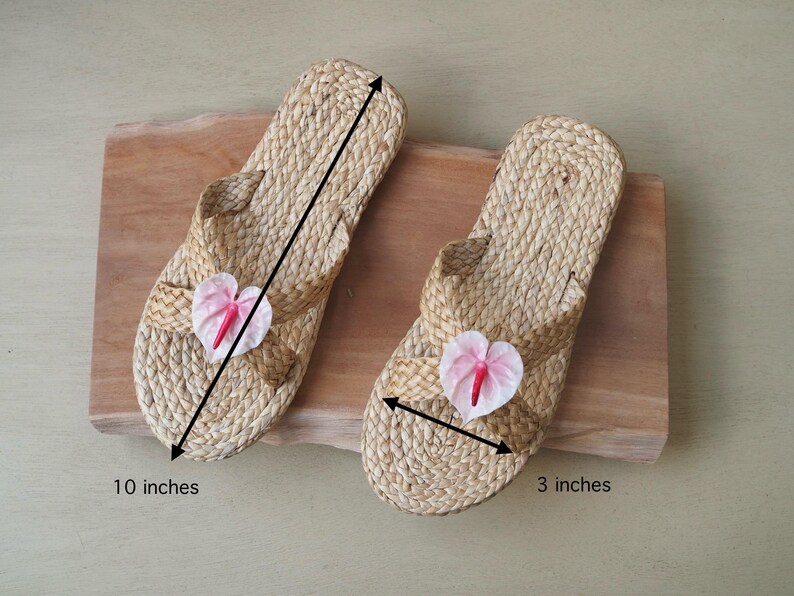 May include: Two pairs of woven straw sandals with pink flower embellishments. The sandals are 10 inches long and 3 inches wide.