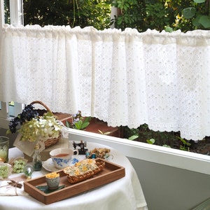 Könnte beinhalten: Ein weißer Spitzenvorhang mit einem gewellten Saum hängt an einem Fenster. Ein Tisch mit einer weißen Tischdecke ist mit einem Teller Essen, einer Tasse Tee und einer Vase mit Blumen gedeckt.