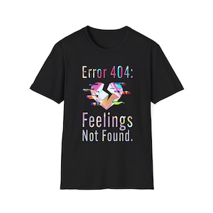 May include: Black t-shirt with the text "Error 404: Feelings Not Found." The design features a broken heart graphic with a glitch effect in shades of pink, yellow, and blue. The shirt is a classic crew neck style.