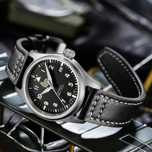 Puede incluir: Un reloj de pulsera de cuero negro con caja plateada y esfera negra. El reloj tiene marcas blancas y una ventana de fecha en la posici&oacute;n de las 3 en punto. La esfera del reloj tambi&eacute;n incluye el texto "Automatic 65ft = 200m".