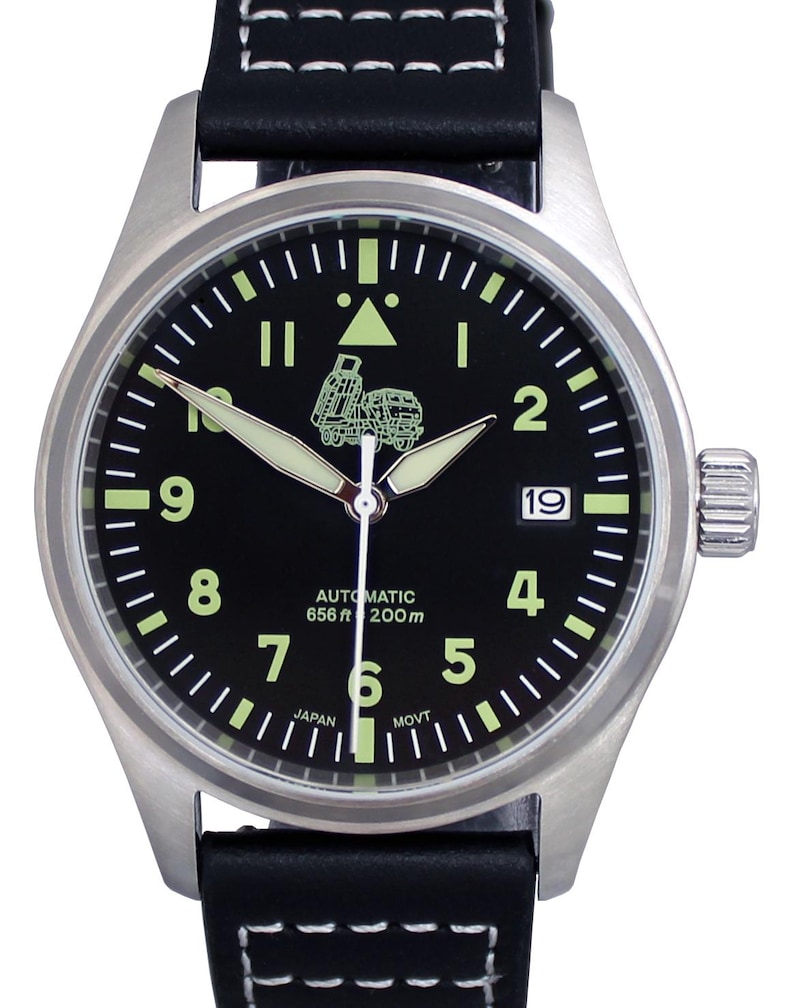 Puede incluir: Un reloj de pulsera con esfera negra, caja plateada y correa de cuero negra. La esfera del reloj tiene marcas blancas y una peque&ntilde;a imagen de un cami&oacute;n. La esfera del reloj tambi&eacute;n dice "Automatic 656 ft 200 m" y "Japan Movt".