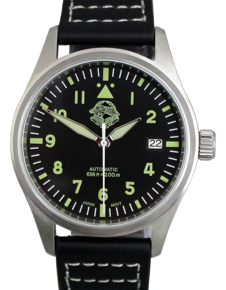 May include: A stainless steel wristwatch with a black face and a black leather strap. The watch face has luminous hands and markers, with the text "AUTOMATIC 656 ft = 200m" and the number "22". The watch includes a date display.