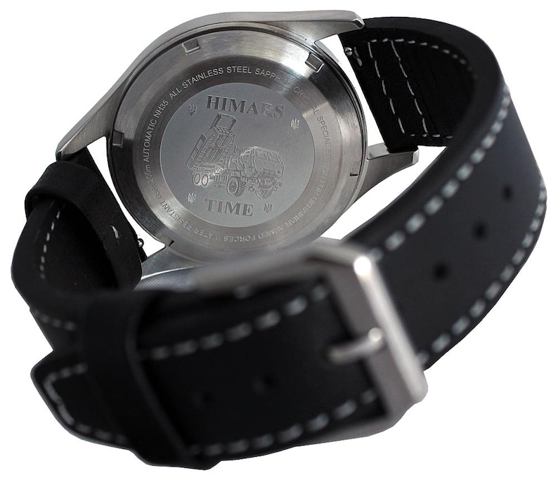 Puede incluir: Vista posterior de una correa de reloj de cuero negro con costuras blancas. La esfera del reloj es de acero inoxidable y presenta el texto "HIMARS" y "TIME" en un dise&ntilde;o circular.
