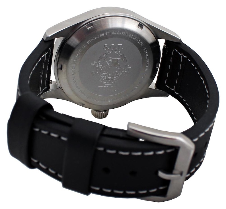 May include: A close-up view of a stainless steel watch with a black leather strap. The watch features a silver case and a black strap with white stitching. The watch's back has engraved text and a logo. The strap is fastened with a silver buckle.