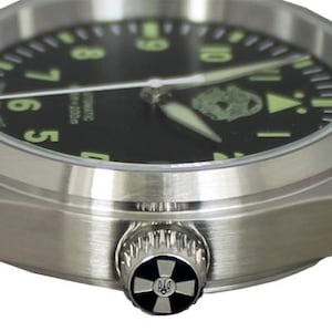 May include: A stainless steel wristwatch with a black face and luminous green numerals. The watch has a black leather strap with white stitching. The watch crown features a decorative design. The watch is an automatic.