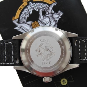 May include: A close-up of a stainless steel watch with a black leather strap and white stitching. The watch face features the text "S.O.F." and "TIME", with an emblem of two animals. It is a special edition for the Ukrainian Armed Forces.