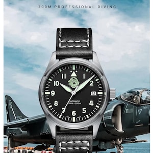 May include: A pilot's watch with a black face, stainless steel casing, and a black leather strap. The watch has luminous hands and markers. The text "PILOT SERIES" is displayed. The background shows a fighter jet.