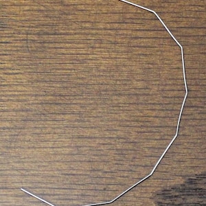 May include: A bent, thin, silver-colored wire in a semi-circular shape. The wire is resting on a brown wooden surface. The wire is made of a single piece and has multiple straight segments.